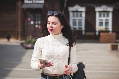 Güneşli bir bahar gününde, elinde telefonla caddede yürüyen güzel bir hippi kız.