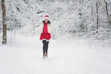Noel elbiseli güzel kız karlı ormanda eğleniyor.