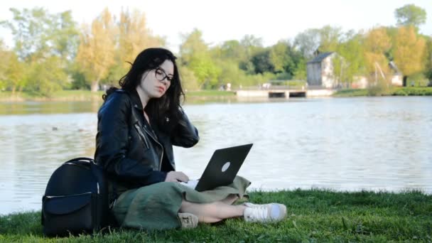 Joven estudiante de trabajo en el portátil en el parque cerca del lago — Vídeos de Stock