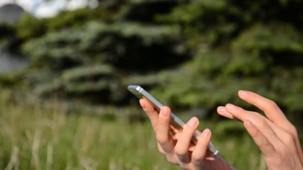 Женские руки и телефон летом на фоне зеленой травы — стоковое видео