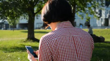 Şirin kadın parkta otururken cep telefonundan mesaj okuyor.