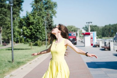 Sarı elbiseli güzel kız güneşli bir sabahta bir yaz parkında yürüyor.