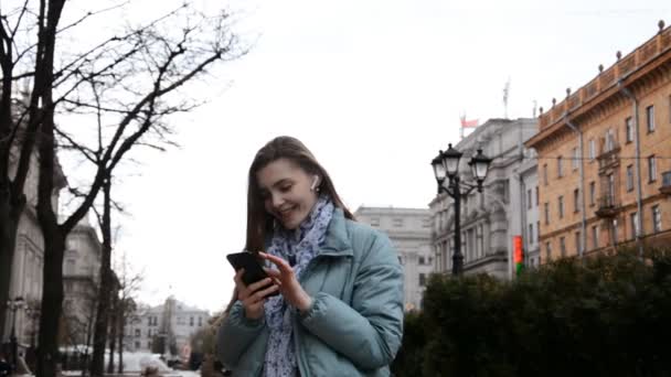 Mujer feliz escribiendo por teléfono móvil al aire libre de pie en el fondo urbano. — Vídeo de stock