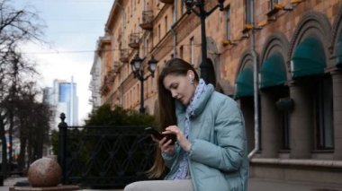 Çevrimiçi iletişim modern gençlik kavramı, genç bir hippi kız bir şehir caddesinde oturur ve bir mesaj yazar.