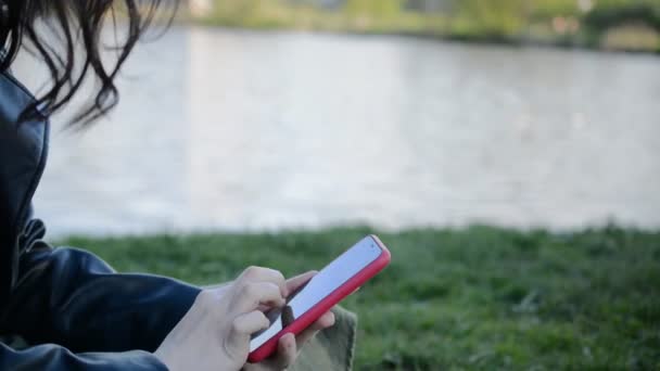 Fechar as mãos femininas digitando mensagens no moderno smartphone vermelho ao ar livre — Vídeo de Stock