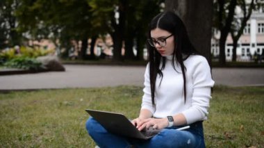 Yeşil çimlerde dizüstü bilgisayarda çalışan güzel bir kadın.