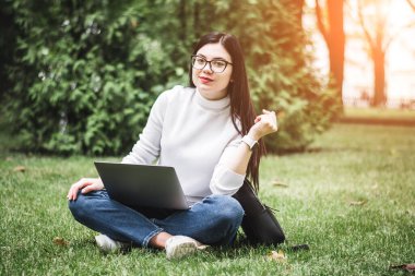 Beyaz Öğrenci Kız yeşil bir parkta dizüstü bilgisayarla çalışıyor.