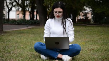 Kafkas üniversiteli kız kampüsteki çimlerde dizüstü bilgisayar kullanmakla meşgul.