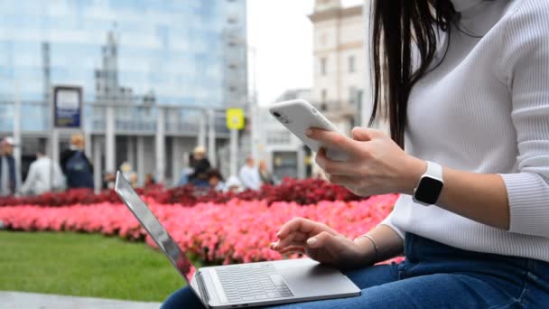 一个手里拿着笔记本电脑和电话的女学生坐在街上 — 图库视频影像