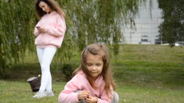 一个快乐的小女孩在春天公园的草坪上玩耍，她的母亲给她写了一封信 — 图库视频影像