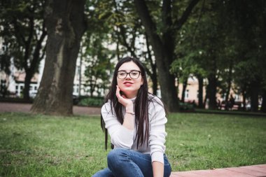 Kot pantolonlu güzel bir kız ve elinde telefonla parkta beyaz bir kazak.