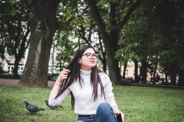 Kot pantolonlu güzel bir kız ve elinde telefonla parkta beyaz bir kazak.