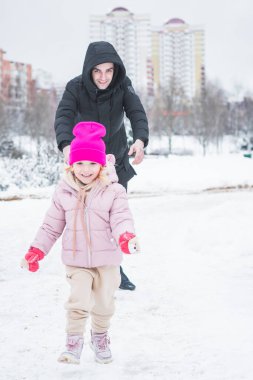 Güzel küçük kız babasıyla kış parkında oynuyor.