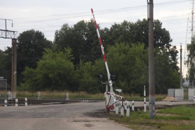 Rus vilayetinin boş düzenlenmiş demiryolu kavşağı asfalt yolda kırmızı beyaz bariyer, bulutlu bir yaz gününde demiryolu manzarası