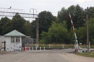 Rus taşrası, istasyon şefinin evi ve asfalt yolda kırmızı beyaz bariyer ile boş demiryolu geçişini düzenledi. Bulutlu yaz gününde demiryolu manzarası.