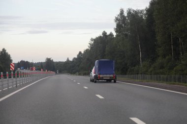 Mavi tenteli tek aksli karavan sürücüsü, asfaltlı banliyö yolunda, orman arka planında bir yaz akşamı, arka manzara...