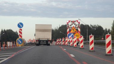 Minibüs, banliyö otobanında yol kenarında hareket ediyor. Yön sinyali, ok işaretleri ve hız limiti 50. Yaz gününde yolun sağ şeridinde güvenlik işareti var.