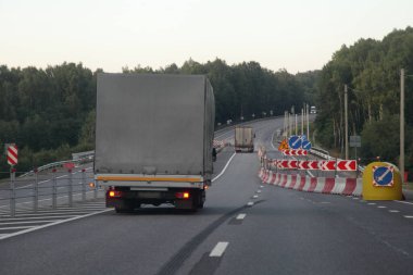 Gri tenteli bir kamyonet daralan bir otoyolda ilerliyor, yol bir yaz akşamı asfaltlanmış bir banliyöde çalışıyor, arka manzara...