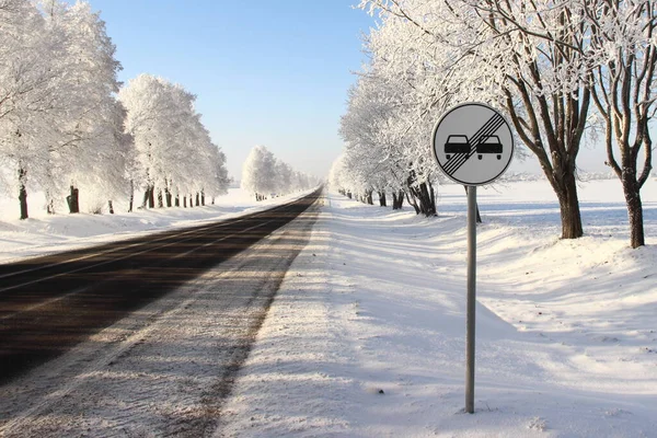 European road sign END ZONE OVERTAKING PROHIBITED on roadside on white snowy trees after snowfall background at Sunny winter day, winter road driving safety