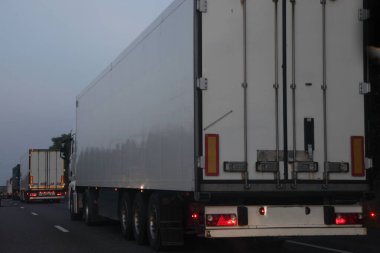 Yarı karavan kamyonları alacakaranlıkta asfaltlanmış akşam yoluna çıkarlar - iç ulaşım lojistiği