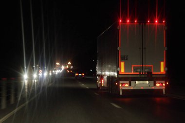 Işıklandırma şeritli yarı karavan kamyonu ve arka tahtada TIR işareti var. Kurumuş asfaltlanmış gece yolunda karanlıkta, arka planda ilerliyorlar. Yerleşik ulaşım lojistiği.