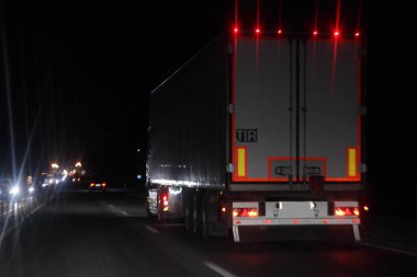 Işıklandırma şeritli yarı karavan kamyonu ve arka tahtada TIR işareti var. Kurumuş asfaltlanmış gece yolunda karanlıkta, arka planda ilerliyorlar. Yerleşik ulaşım lojistiği.