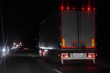 Semi trailer truck with lighting reflection stripe on rear board move on dry asphalted night road in dark, back view - intrenational transportation logistics clipart