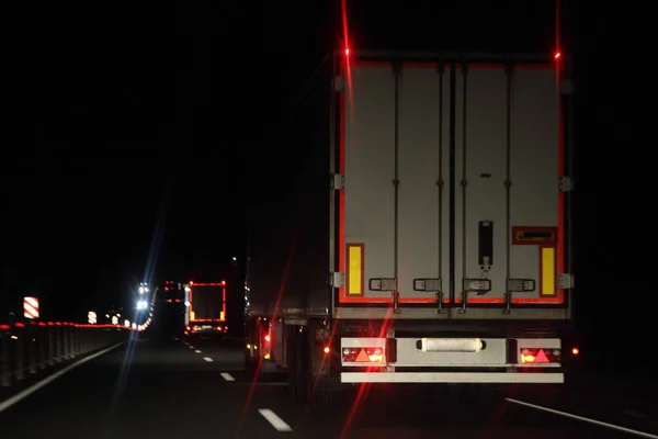 Semi trailer truck with lighting reflection stripe on rear board move on dry asphalted night road in dark, back view - intrenational transportation logistics