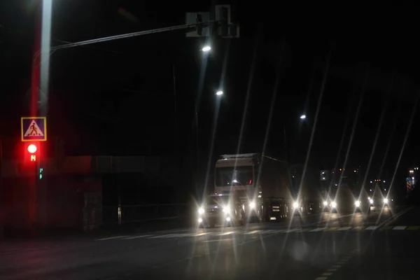 Cars with lighting head lights stopped on red traffic light on dry asphalted night road in dark, frint view - night driving safety