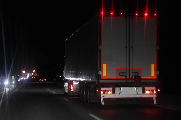 Semi trailer truck with lighting reflection stripe on rear board move on dry asphalted night road in dark, back view - intrenational transportation logistics