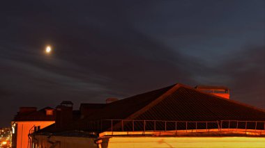 Bulanık bir gökyüzü, bulanık ay arkaplanı ve manzaralı gece manzarası olan güzel Avrupalı kırmızı fayanslı aydınlık ev çatısı.