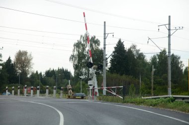 Rus ülkesi, asfalt yolda kırmızı beyaz bariyerle boş demiryolu geçişini, bulutlu yaz gününde demiryolu manzarasını düzenledi.