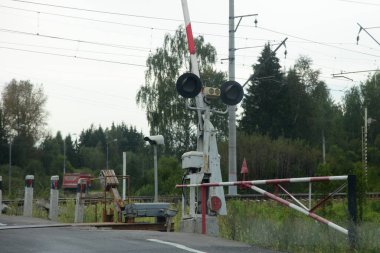 Rus vilayeti, asfalt yolda kırmızı beyaz bariyerli boş demiryolu geçidini düzenledi, bulutlu yaz gününde demiryolu manzarası