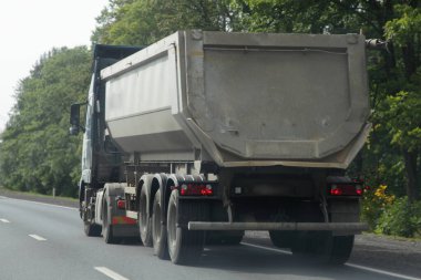 Bir adet gri ağır damperli kamyon, yarı karavanı boş banliyö kavşağında asfaltlanmış otoyolda yaz günü arka planda, arkadan görüş lojistiği, toplu kargo taşımacılığı.