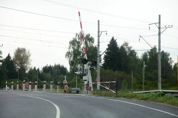 Rus ülkesi, asfalt yolda kırmızı beyaz bariyerle boş demiryolu geçişini, bulutlu yaz gününde demiryolu manzarasını düzenledi.