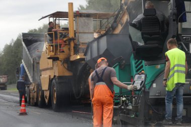 Otoyol onarımı, asfalt temizleyici, sıkıştırıcı buz pateni pisti ve Kafkasyalı yol işçileri yaz günü gri gökyüzü ve yeşil orman arka planında, yol yapımı endüstriyel makineler teknolojisi