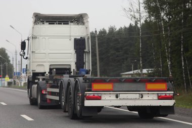 Beyaz boş kamyon konteynır taşıyıcı platformu yaz günü asfaltlanmış otoyolda hareket ediyor. Arka taraf görüntüsü uluslararası lojistik, kargo taşımacılığı, taşımacılık endüstrisi...