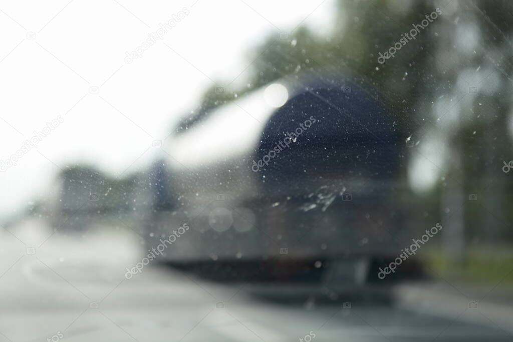 Poor visibility of the tired driver through the dirty windscreen, blurred silhouettes of trucks on suburban highway road, driving safety