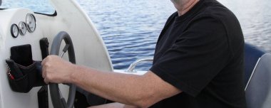 Suda yüzen motorlu tekne direksiyonu tutan tişörtlü bir adam yaz günü su arka planında kontrol cihazları olan bir kabin iç gösterge paneli, açık havada tekne gezintisi.