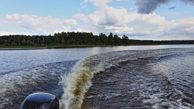 Bir sürat teknesi nehir suyunda döner yeşil çimenli arka planda çember keelwater yolu ile yaz günü, köpüklü trenin dikiz manzarası motorlu teknenin kıç tarafından tek motorlu olarak uyanıyor.