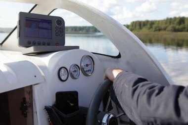Yüzen motorlu tekne direksiyonunda el ele tutuşan bir adam, yaz günü su ve nehir kıyısı arka planında tekne gezisinde kontrol cihazları olan bir kabin iç gösterge paneli.