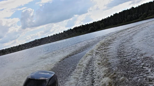 A speedboat fast turns off on the river on forest shore background at summer day, back view on the transom Wake in the water from the stern of motor boat with single powerful outboard motor
