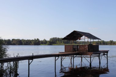 Boş ahşap balkon cambaz ayaklıkları üzerinde ahşap köprü yolu perspektif nehir suyu, mavi gökyüzü ve ufukta yeşil orman ağaçları yaz günü arka plan, açık hava eğlencesi, güzel nehir manzarası