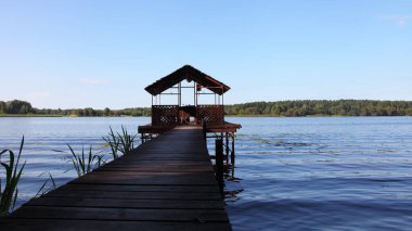 Boş ahşap balkon ayaklıklar üzerinde ahşap yol perspektif nehir suyu, mavi gökyüzü ve ufukta yeşil orman ağaçları yaz günü arka plan, açık hava tatil köyü, güzel nehir manzarası