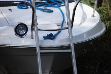 Beyaz plastik motorlu tekne güvertesi merdiven döşeli, far lambalı nehir kıyısında su kenarında yeşil çimenli arka planda güneşli yaz günlerinde, açık hava tatillerinde