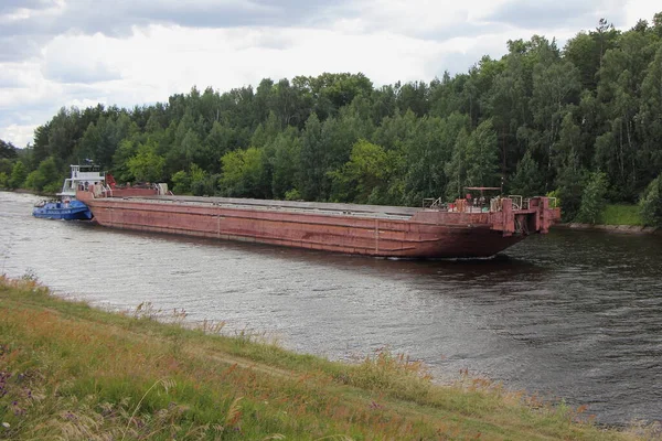 Big old empty barge with Pusher vessel tugboat floats on Moscow Canal water at summer day, cargo shipping on the river, Russian logistics of cargo transportation by water transport