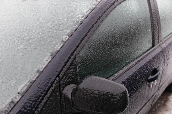 Ice covered car side mirror, glass, windscreen and side door, close up front side view of an icy vehicle on a winter day after freezing rain in Russia