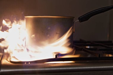Paslanmaz çelik mutfak gaz ocağında eski bir tava. Turuncu büyük alevler yanıp sönüyor. Kapalı alanda yangın önleyici.