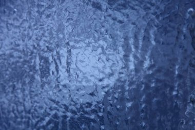 Buz yağmuru, yarı şeffaf koyu mavi cam yüzeyine bulanık buz damlaları, arka plan için soyut kış dokusu.