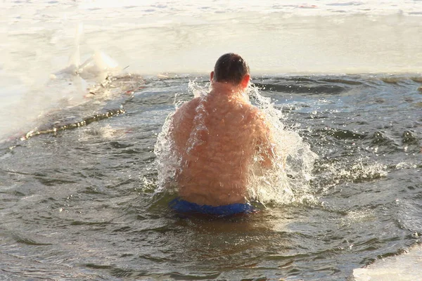 冬のアイススイミングスポーツ 水泳トランクスのヨーロッパ人男性は 晴れた霜の冬の日に水しぶきと氷の穴の水で泳ぐ 健康的なライフスタイル — ストック写真